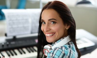 Close-up of smiling wonderful woman playing synthesizer on notes. Beautiful girl wearing...