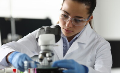 Adult caucasian beauty woman chemist in protective glasses looking at microscope against chemistry...