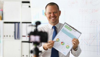 Portrait of smiling blogger in classic suit and tie showing statistics data with graphs charts...
