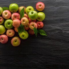 group of green and red apples on a black stone background seen from above and in square format