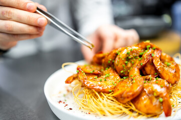 chef cooking a plate of glazed shrimp on crispy noodles with chopsticks, highlighting the art of...