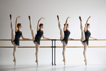 Young girls, ballet dancers showing grace and flexibility, standing next to barre and training,...