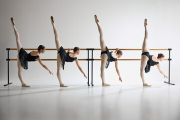 Elegance in motion. For flexible teen girls, ballet dancers training next to barre equipment against grey studio background. Concept of ballet, art, dance studio, classical style, youth