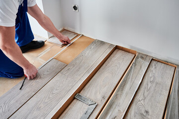 Close up of man construction worker checking distance from wall to laminate board. Male builder using tape measure while installing laminate flooring in apartment under renovation.