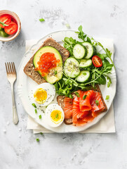 Healthy breakfast featuring avocado, egg, sandwiches with salmon on white plate and coffee.