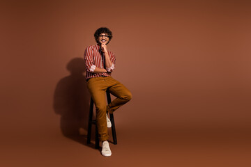 Full size photo of nice young man sit stool think wear striped shirt isolated on brown color background