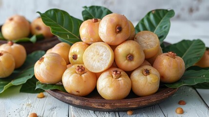   A wooden bowl holds a pile of apricots on a white table, nearby are leaves