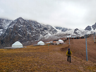 Yurts on a mountain plateau with snowy peaks in the background, under a cloudy sky