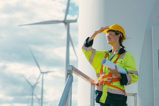 female engineer working outdoor with safety at wind turbines clean energy power station background, worker people with renewable energy technology for future concept.
