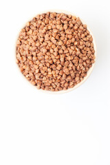 Uncooked, brown buckwheat grains in bowl on white background. Top view. Space for a text - obrazy, fototapety, plakaty
