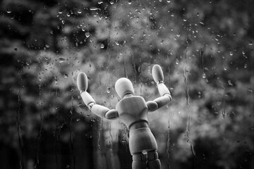 Mental health problem concept. Wooden mannequin by the window in the rain. Sadness, loneliness, depression or seasonal affective disorder - obrazy, fototapety, plakaty