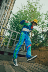 Young boy wearing vibrant '90s inspired sportswear in blue color, yellow panama and casual sport shoes, walking outdoors. Concept of 90s, fashion, youth culture, old-style trends