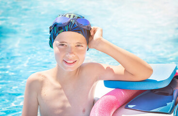 Happy child (boy) in cap, sport goggles ready to learns professional swimming with pool board, swim noodles and fins for swimming. Kid enjoying water in swimming pool. Healthy lifestyle. - obrazy, fototapety, plakaty
