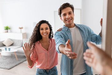 Happy young couple inviting people to enter home, shaking hands
