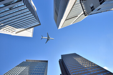 晴天の日の新宿高層ビル街の上を飛ぶ旅客機