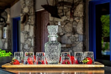 Rustic wooden tray adorned with a elegant carafe and small glasses, delicately arranged amidst a bed of fresh strawberries. Inviting and picturesque appeal.