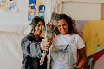 Artist friends smiling and showing their paint brushes