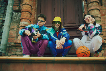 Friends meeting outdoors, boys and girl wearing stylish vivid sportswear, sunglasses and comfortable sport shoes, posing against vintage door background. Concept of 90s, fashion, youth culture