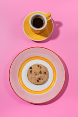 Chocolate chip cookie on a bright plate, pink backdrop with a cup of coffee.