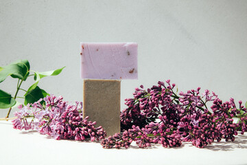 A bar of natural soap with lilac flowers on a concrete background. Cosmetics from natural ingredients, herb. Front view - obrazy, fototapety, plakaty