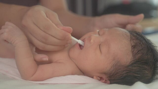 Closeup of hand cleaning tongue in the mouth of a newborn child with a cotton swab