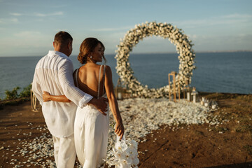 wedding on a cliff with a bride in a white dress and a groom in a white shirt on the beach with...