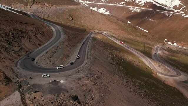 Cars drive along a mountain serpentine, a winding road in the mountains, aerial view. Top down view of highway on mountainside