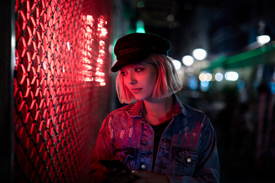 Young woman using smartphone by neon-lit city wall at night