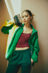 Chic sportswear elegance. Beautiful young girl with vibrant makeup wearing green tracksuit, posing with boombox. Concept of 90s, fashion, youth culture, old-style trends