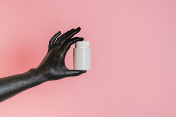 Black painted elegant woman's hand on her skin with white cosmetic bottle. High Fashion art...