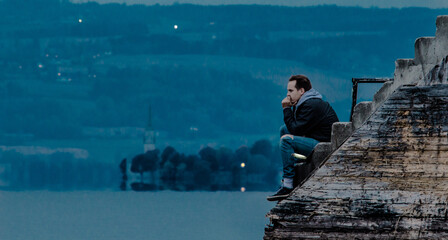 Man sitting at the dock in twilight, thinking about the meaning of life. Lake, headland with church...
