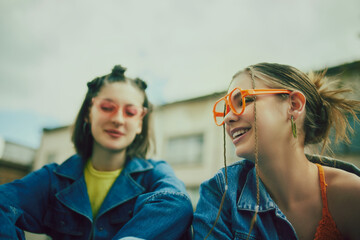 Young people, stylish girls wearing denim clothes and and colorful accessories. Chilling on urban rooftop on a daytime. Concept of 90s, fashion, youth culture, old-style trends