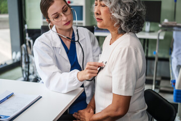 Caucasian woman checks an Asian elderly woman's heartbeat using a stethoscope. They communicate...