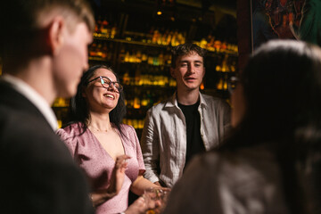 Happy woman tells funny story to close friends in bar. Brunette lady with eyeglasses communicates...