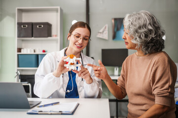  Caucasian woman assists an elderly Asian woman with a herniated disc, using a human anatomical...