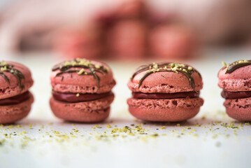 Raspberry macarons topped with chocolate drizzle and gold flakes, arranged in a row for an elegant presentation