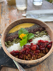 smoothie bowl of fruit in a wooden bowl on table, berries, nuts and mango sauce