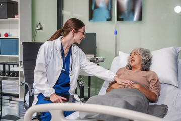 Obraz premium Caucasian female specialist doctor attends to an elderly Asian female patient in a hospital bed, providing medical care and support.