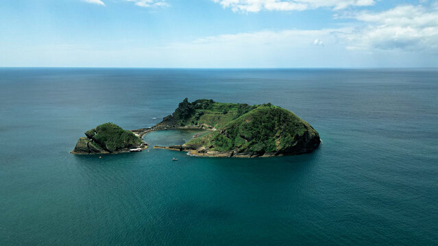 An aerial view of a small green island in the sea. The photo was taken in the Azores Islands.