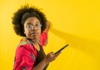 mujer joven afro mirando al frente y usando lentes mientras sostiene su movil en sus manos 
