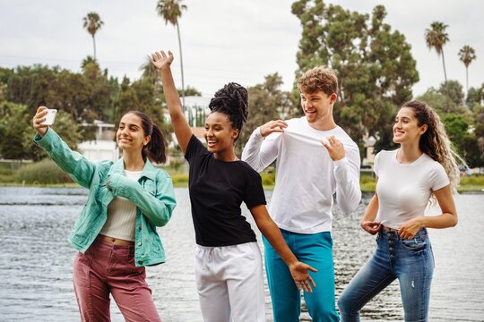 Diverse friends taking selfies by the lake, summer casual fashion