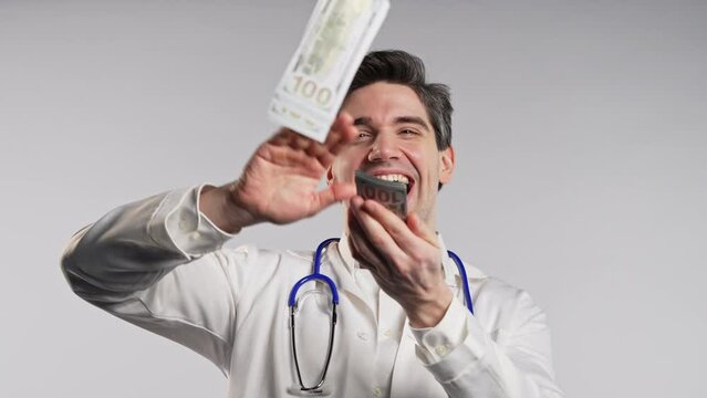 Rich doctor man scatters money. Handsome medical health care worker in white coat overspend USD dollars banknotes. 