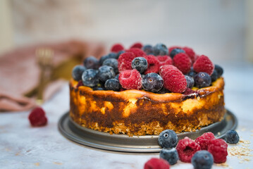 Homemade cheesecake topped with fresh blueberries and raspberries, served on a rustic table.
