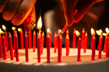 Detalhe de duas mãos acendendo várias velas sobre um bolo de aniversário.