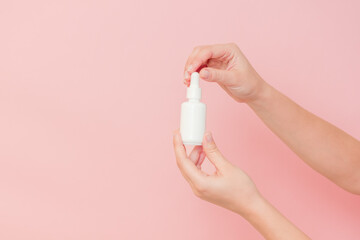 Glass cosmetic bottle for serum (hyaluronic acid and collagen) in hand on pink background. Beauty...