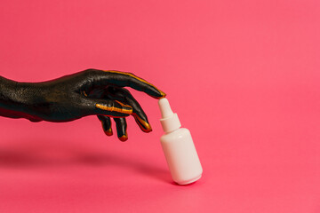 Black and gold painted elegant hand on skin with cosmetic unbranded bottle. Luxury, high fashion cosmetic products concept