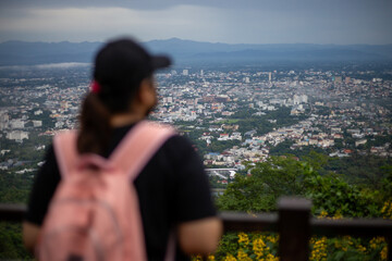 Fototapeta na wymiar High-angle view of the city, a blurred woman standing and watching the city in the foreground. Many buildings in Chiang Mai, Thailand city viewpoint