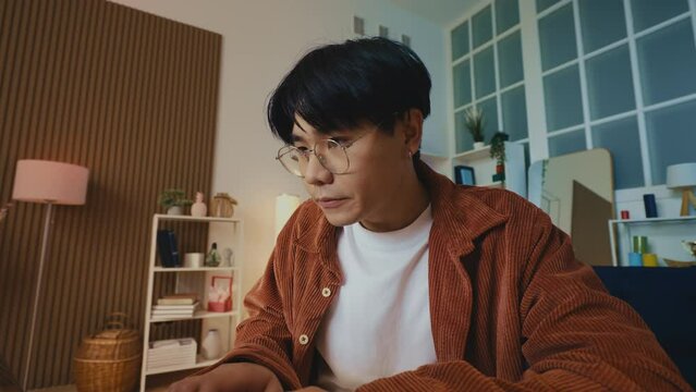 Young busy Asian man programmer typing fast on laptop, working online from home
