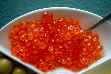Red caviar in a white plate with olives, cheese and spoon