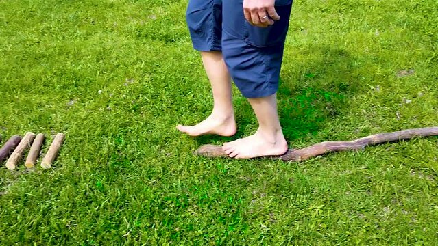 Footage with a close-up on the feet of a Caucasian man walking barefoot: he walks first on a branch then on small logs arranged horizontally, then dry leaves and finally straw.